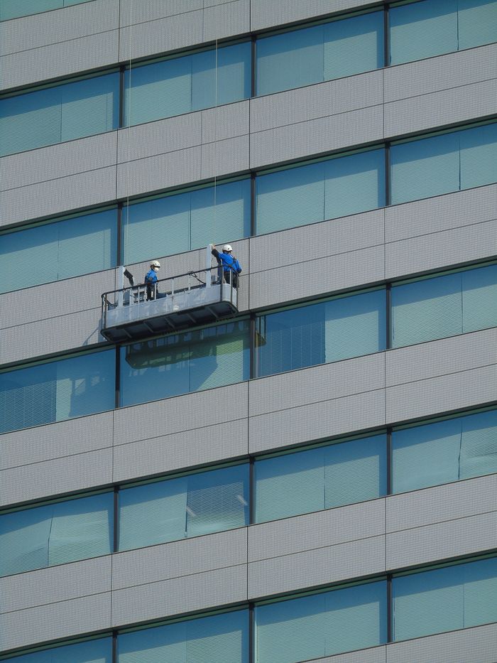 Two workers are cleaning the windows of a modern glass building facade from a suspended platform.